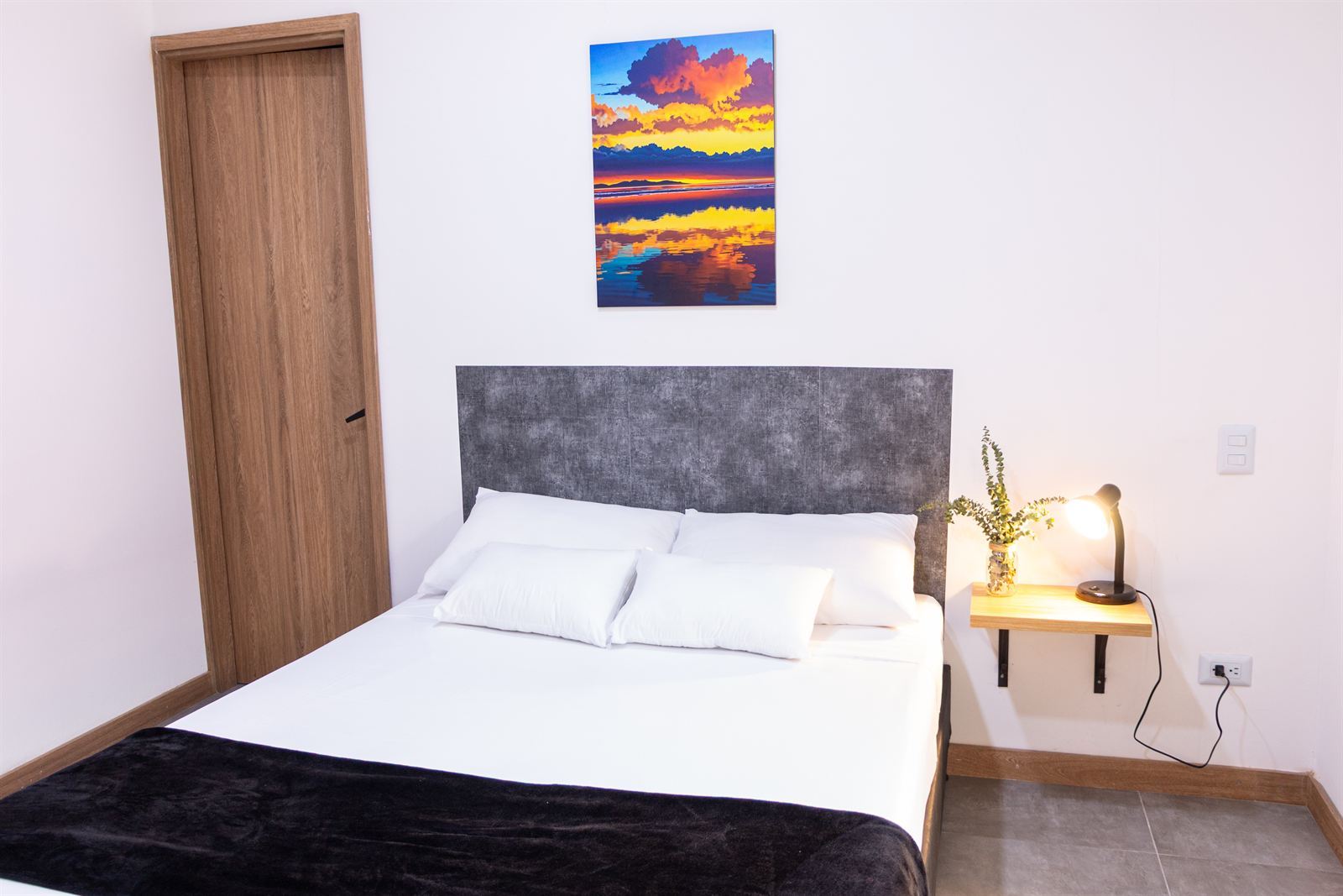 Doppelbett mit gepolstertem grauem Kopfteil und Sonnenuntergangs-Bild darüber — Doble Externas Con Balcón