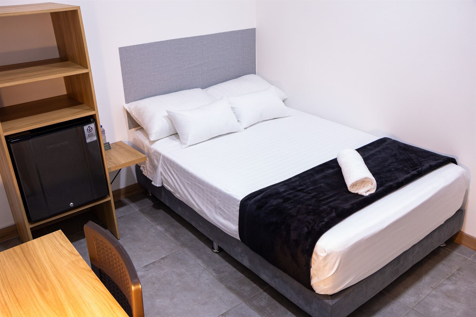Cama doble con manta negra, estante de madera con nevera y escritorio con silla — Doble Superior Internas