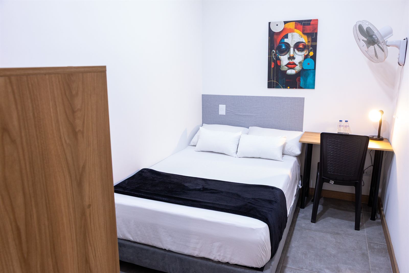 Cama doble con cuadro decorativo abstracto sobre el cabecero, ventilador de pared y escritorio con lámpara — Doble Superior Internas